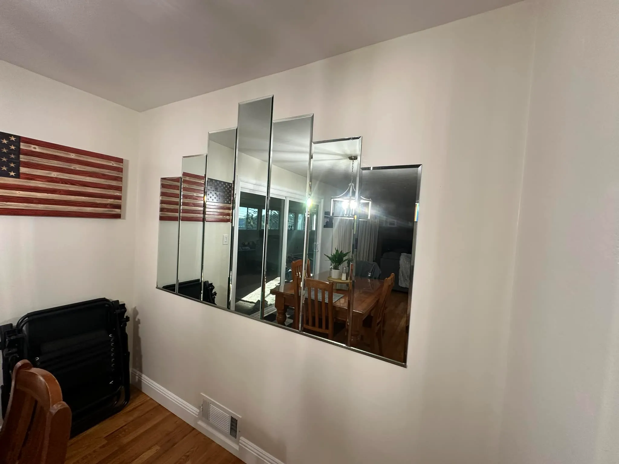 A set of five rectangular mirrors arranged in a staggered pattern on a white wall, reflecting a dining area with a wooden table, chairs, and a light fixture.