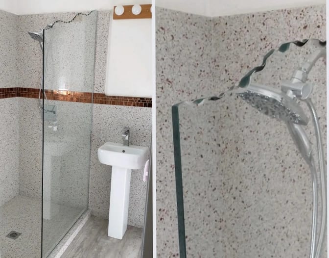 A bathroom with a Custom Shower Panel featuring a wavy, chipped-top glass divider, positioned beside a sink and a wall-mounted showerhead.