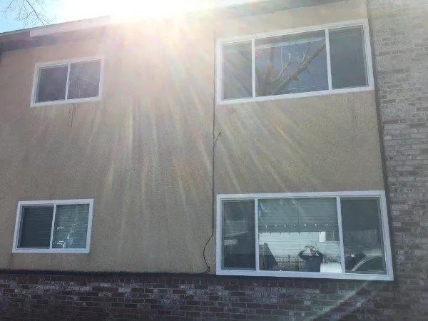 A person takes a photo of a two-story building exterior with sunlight streaming down, showing three windows and some brickwork at the bottom.