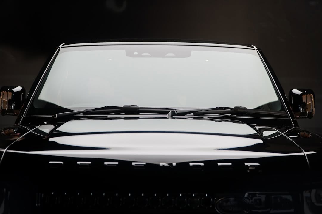Front view of a black Land Rover Defender with visible windshield, hood, and part of the grille under studio lighting.