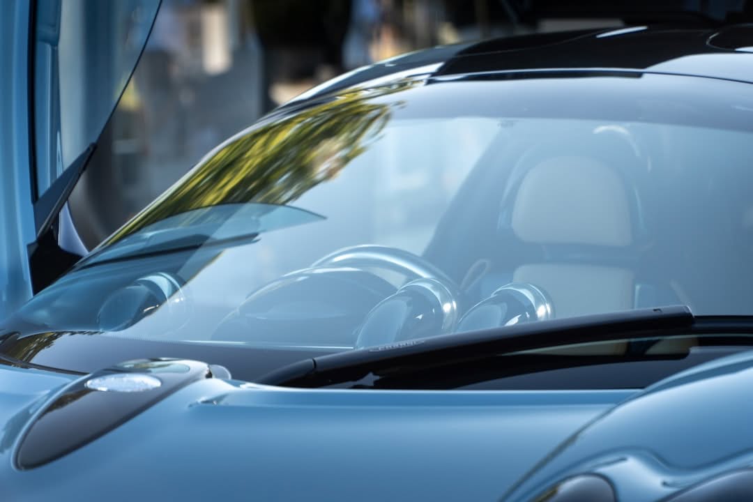 Close-up view of the front windshield and dashboard of a modern blue sports car, with reflections of trees visible on the glass.