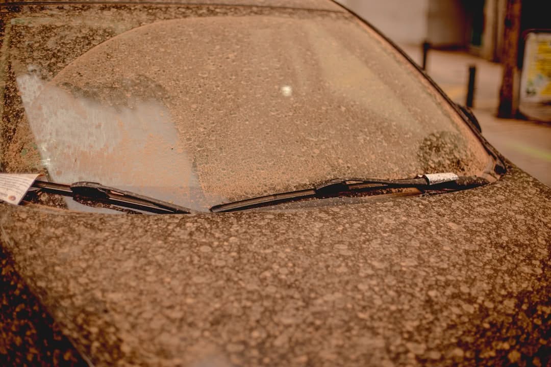 A car covered in a thick layer of dust with its windshield wipers visible and a parking ticket on the windshield.